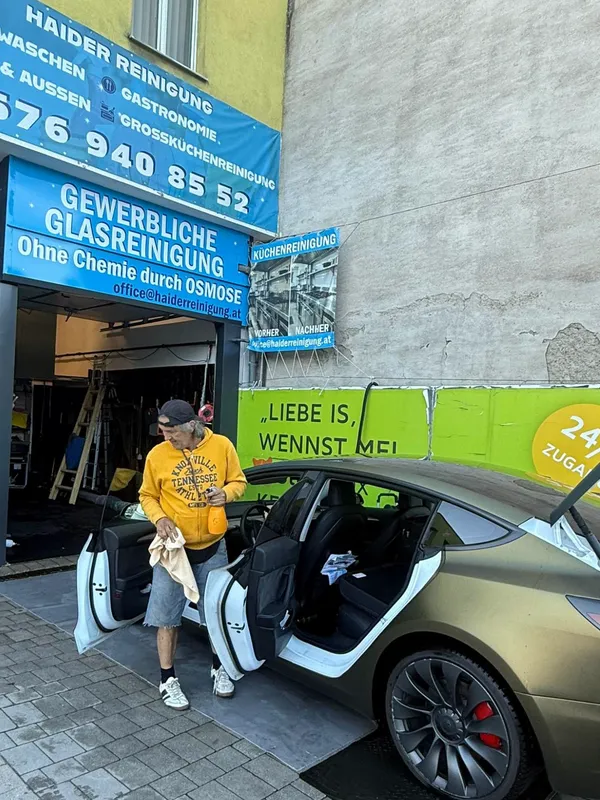 Mitarbeiter mit Mikrofasertuch und Sprühflasche bei der Detailarbeit am Tesla