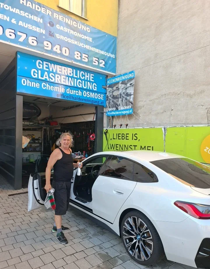 Mitarbeiter reinigt den Türeinstieg eines weißen BMW vor der STEAMWERK-Werkstatt in Meidling