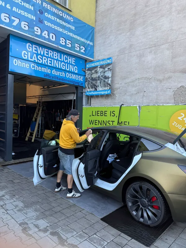 Mitarbeiter reinigt die Seitenscheibe eines Tesla von Hand streifenfrei